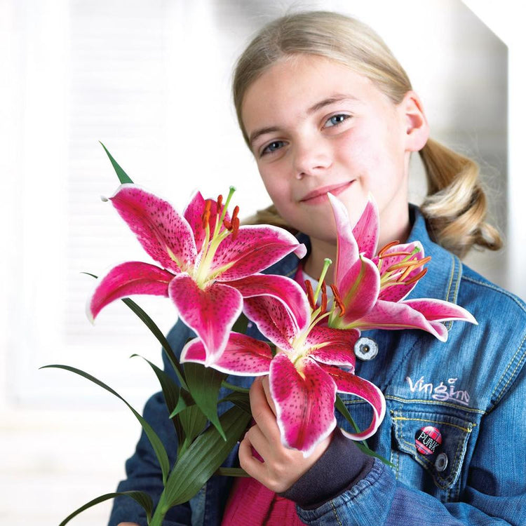 Oriental lily Colorado being held by a young girl to show the impressive size of the fragrant, deep pink flowers.