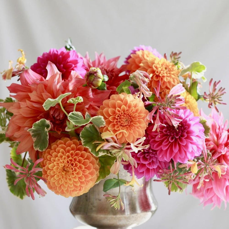 A detail photo of a flamboyant tabletop arrangement of pink and orange dahlias, featuring the varieties Maarn, Candiflora and Penhill Dark Monarch.