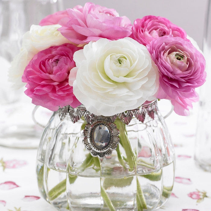 A tabletop bouquet of pink and white ranunculus in a clear glass vase.